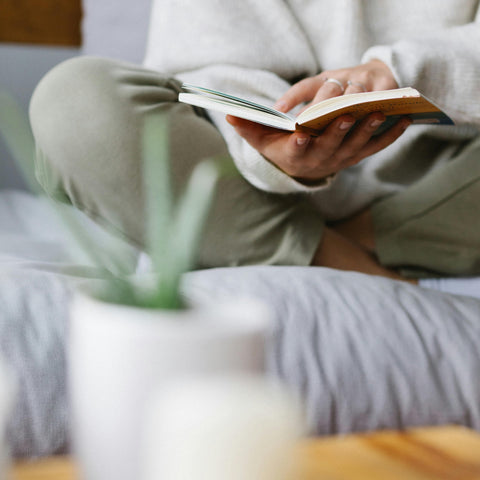 Individual sitting in loose white clothing cross legged, reading a book